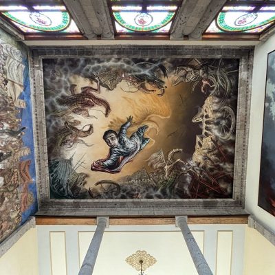 A dramatic ceiling mural depicts a scene of mythical creatures and warriors in battle. At the centre, a warrior twists in midair. The mural is framed by ornate architectural moldings and colourful stained glass windows.
