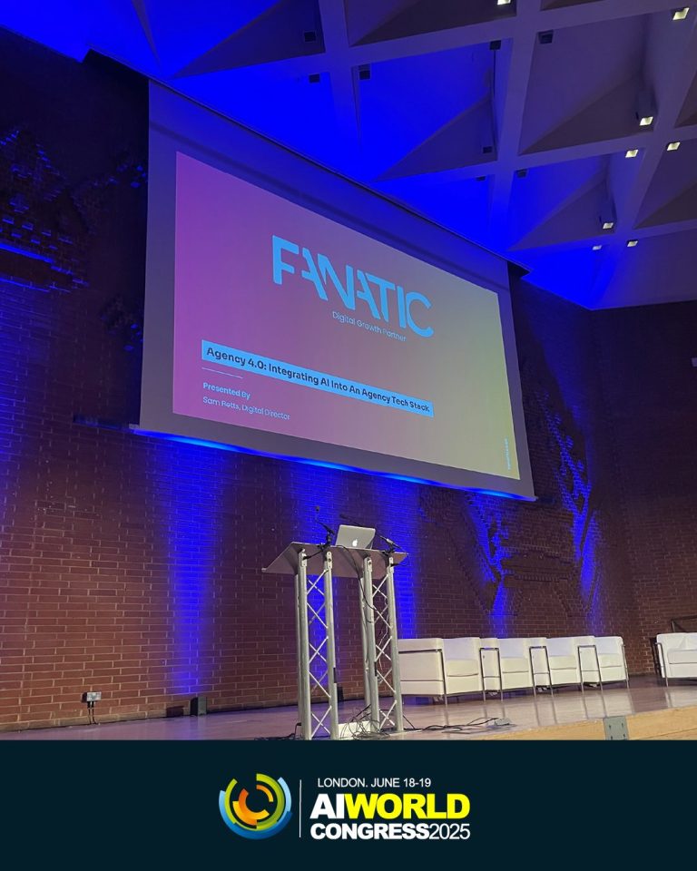 A stage with a podium and white, modular armchairs are set up in front of a large screen displaying 